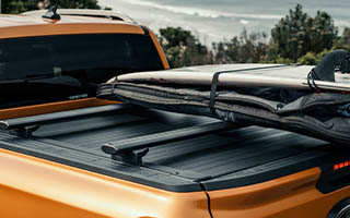 Detailansicht von einem Mountain Top Evo Rollo mit Querträger und Surfbrett auf einem Ford Ranger am Strand