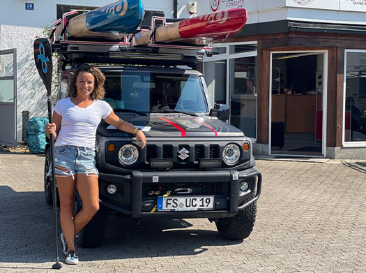 Brand ambassador Susanne Lier in front of her converted Suzuki Jimny and SUP roof rack with 3 SUP boards on the roof